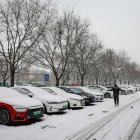 Un hombre transita por una calle en donde los carros aparecen estacionados y cubiertos bajo un manto blanco y congelado, en Pekín, este miércoles 13 de diciembre de 2023.