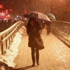 Una mujer al caminar con dificultad sobre un puente peatonal elevado y bajo una fuerte torementa de nieve en Shanghái (China).