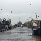 Una persona recorre el muelle de Santa Mónica sosteniendo un paraguas en medio la tormenta azota el sur de California.