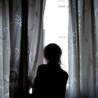 Una mujer observando a través de la ventana de su vivienda mientras permanece confinada por la crisis del coronavirus