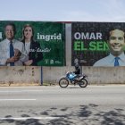 Una persona en una motocicleta pasa junto a un cartel de campaña electoral este domingo, en Santo Domingo (República Dominicana).