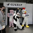 Activistas vestidos como un pollo, un cerdo y una vaca sostienen carteles que dicen "Cada animal es alguien", frente a una tienda que vende carne de ballena en máquinas expendedoras.