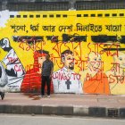 Varias personas caminan junto a un mural en una calle de Daca.