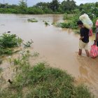 personas cruzan con sus pertenencias por un río en medio de las inundaciones causadas por la tormenta tropical Sara en El Progreso, Honduras.