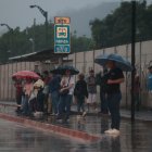 Decenas de usuarios con paraguas permanecen la tarde de este 12 de diciembre a un costado de las vías.