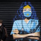 Un chico con mascarilla pasa delante de un mural en Pristina (Kosovo)