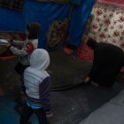 Una mujer palestina desplazada internamente limpia su tienda con sus hijos.