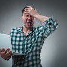 Portrait of young handsome man using laptop, wearing plaid shirt. Studio shot. Emotions