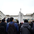 Un grupo de la comunidad vietnamita de Roma reza ante la estatua de Juan Pablo II afuera del hospital Gemelli, donde está hospitalizado el Papa.