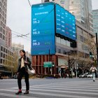 Una persona camina por una calle cerca de las pantallas que muestran las cifras de la bolsa de valores en China.