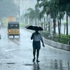 Un hombre que sostiene un paraguas viaja por una calle mientras llueve en Chenna.