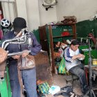 Oswaldo Cujilema (de pie) cose la planta de una zapatilla en su local “Cosedora Los Andes”, donde continúa el legado de su abuelo zapatero.