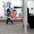 Una mujer iraní con velo se sienta en una estación de autobuses junto a un mural antiestadounidense cerca de la antigua embajada de Estados Unidos en una calle de Teherán.