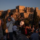Los turistas disfrutan de una puesta de sol mientras están sentados en la colina del Areópago con vistas a la antigua Acrópolis de Atenas.