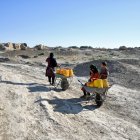 Carencia. Una mujer afgana con sus hijos toma un descanso mientras transportan bidones de agua en carretillas en el pueblo de Bolak.