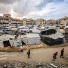 Un hombre y niños caminan junto a tiendas de campaña que albergan a personas desplazadas por la guerra, instaladas cerca de la mezquita Sheikh Hamad bin Khalifa Al-Thani, gravemente dañada.