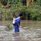 Fotografía del 29 de octubre de 2025 de un hombre cruzando un río crecido mientras carga a un niño, en el poblado de Guama en Santiago de Cuba (Cuba).
