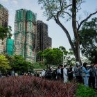 Varias personas dejan flores como tributo a las víctimas del incendio del complejo residencial Wang Fuk Court, en el fondo.