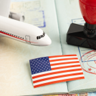 Referencial. Pasaporte con sellos de entrada y salida, junto a una bandera de EE.UU. y un avión en miniatura, simboliza las tensiones migratorias entre Tailandia y Estados Unidos.