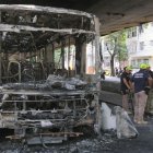Bomberos observan los restos de un autobús incendiado por supuestos integrantes de una facción criminal, en respuesta a la muerte de Claudio Augusto dos Santos en Río de Janeiro