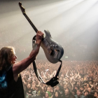 Integrante de Iron Maiden levanta su guitarra ante miles de fanáticos durante un concierto, en una escena que refleja la energía de la banda británica en vivo.