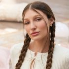 Fotografía promocional de Yami Safdie en un ambiente interior con tonos pastel. La artista aparece sentada en el piso, con trenzas, blusa blanca tejida y una estética visual vinculada al universo de Querida Yo.