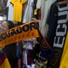 Una clienta sostiene una bufanda tricolor con el lema "Ecuador, sí se puede" en un local repleto de prendas alusivas a la selección, en plena fiebre por la moda mundialista.