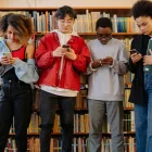 Estudiantes consultan sus teléfonos en una biblioteca, mientras Noruega restringe el uso de inteligencia artificial para menores de 6 a 13 años.