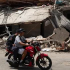 Personas transitan en motocicleta frente a edificios colapsados por los terremotos en Catia La Mar, Venezuela.