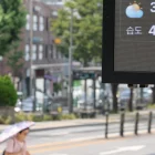 Un tablero digital muestra 38 °C en una calle de Pyongyang, mientras un transeúnte se protege del sol con sombrilla en plena ola de calor.