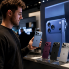 Una persona sostiene uno de los nuevos modelos de iPhone mientras observa otros dispositivos exhibidos en una tienda de tecnología.