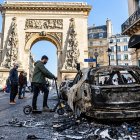 La gente pasa junto a un coche calcinado tras los enfrentamientos entre la policía antidisturbios y los manifestantes en París.